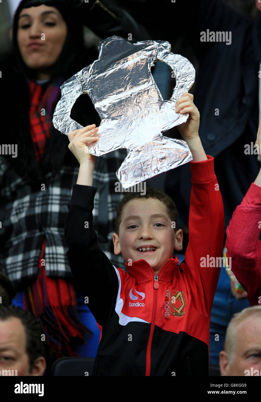 A young Milton Keynes Dons fan holds up a cardboard FA Cup in the