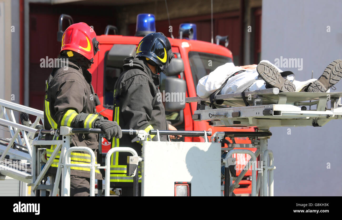 brave firefighters on the fire truck cage save the wounded person with the stretcher Stock Photo