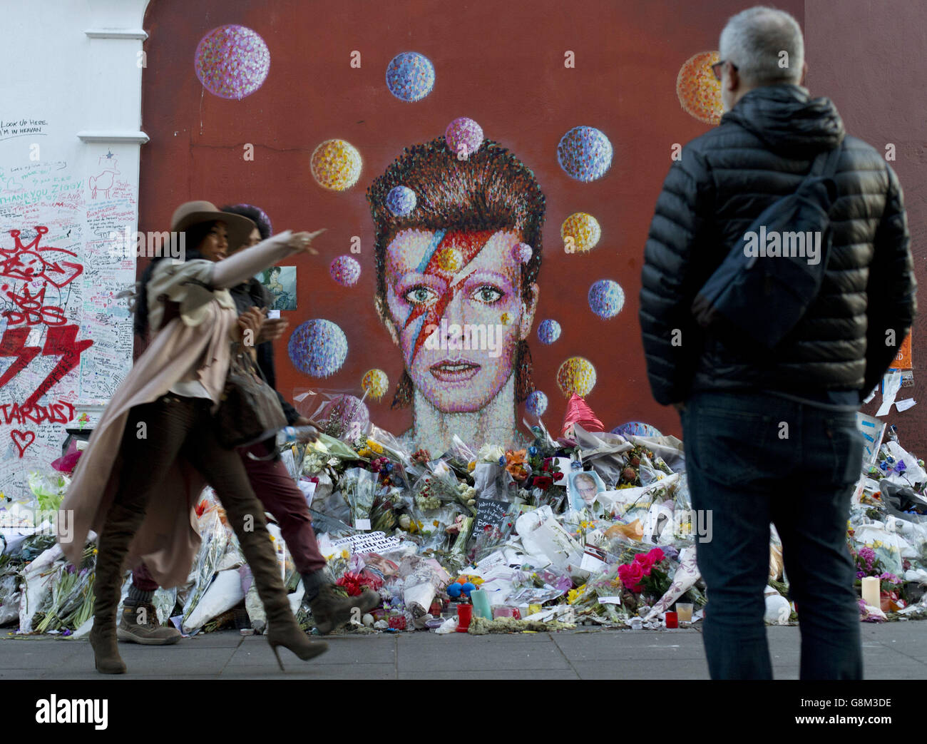 People walk past a mural of David Bowie, who died of cancer on January 10 2016, in Brixton, London, on World Cancer Day. Stock Photo