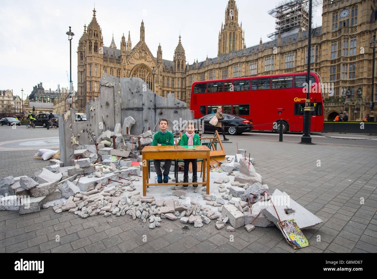 Abdallah, 12, and Dania, 10, whose school was bombed in Aleppo in Syria sit in a mock up of a destroyed classroom outside the Houses of Parliament in Westminster, London, at a Save the Children photocall to highlight the need for education for refugee children ahead of the London Syria Conference. Stock Photo