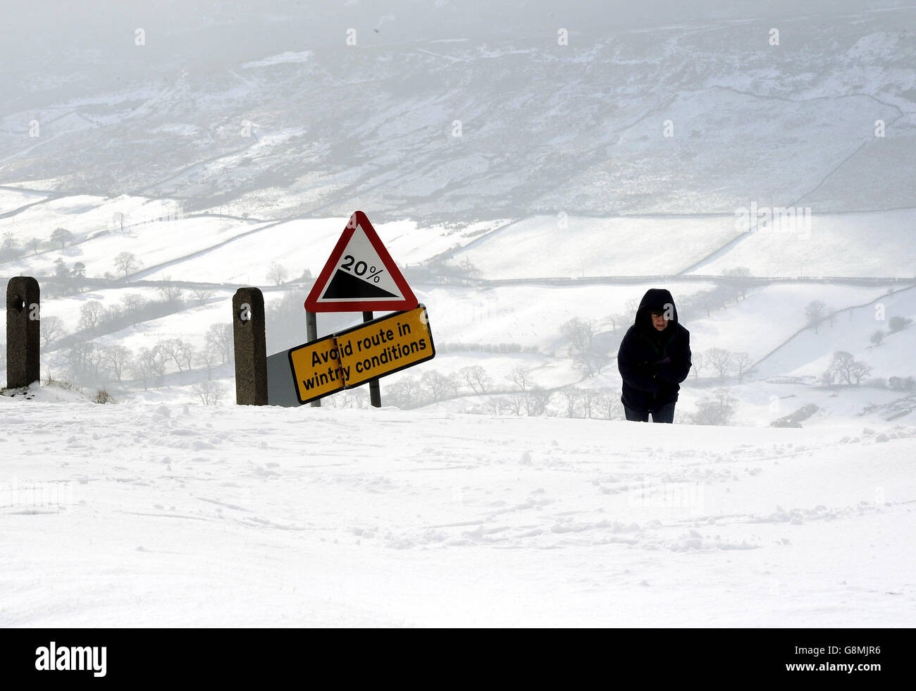 A walker tackles the road between Hutton-le-Hole and Farndale in the North York Moors after heavy snowfall. Stock Photo