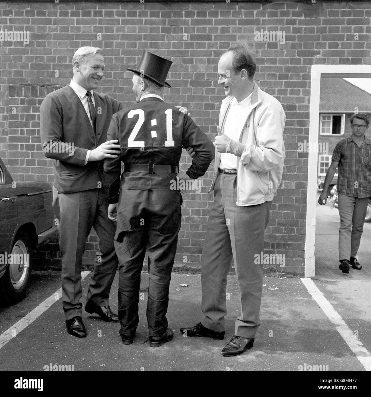 A West Germany fan dressed as a chimney sweep (a German symbol of good luck) is congratulated on his prediction for the World Cup Final scoreline by team advisor Bert Trautmann (l) and team doctor W. Gerhardt (r) as they meet on the morning of the final outside the team's hotel Stock Photo
