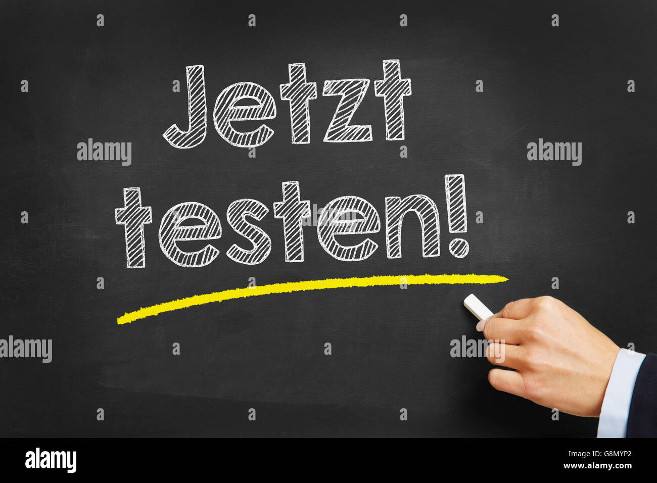 Hand with chalk writing in German 'Jetzt testen!' (test it now) on a chalkboard Stock Photo