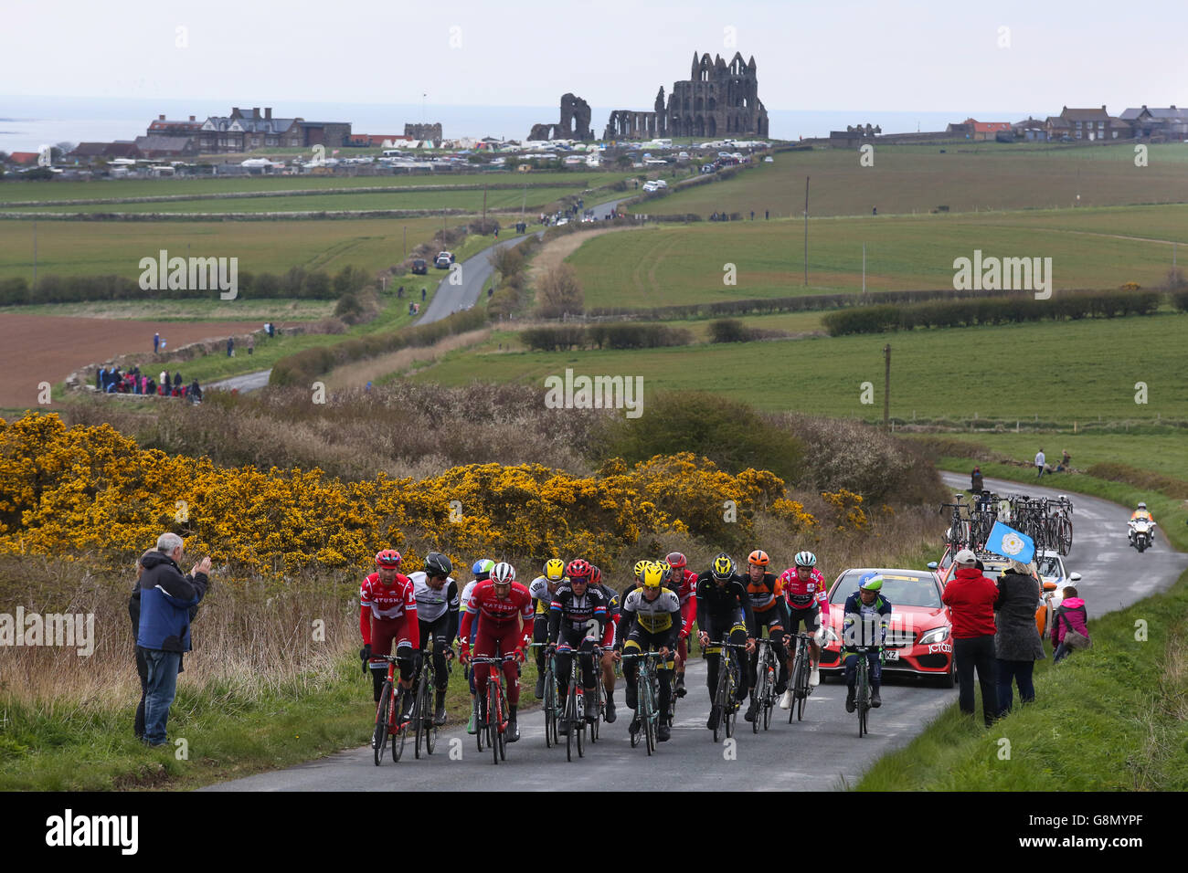 Whitby, UK. The peloton, with the famous abbey behind them, makes it's way out of Whitby during the third and final stage of the Stock Photo