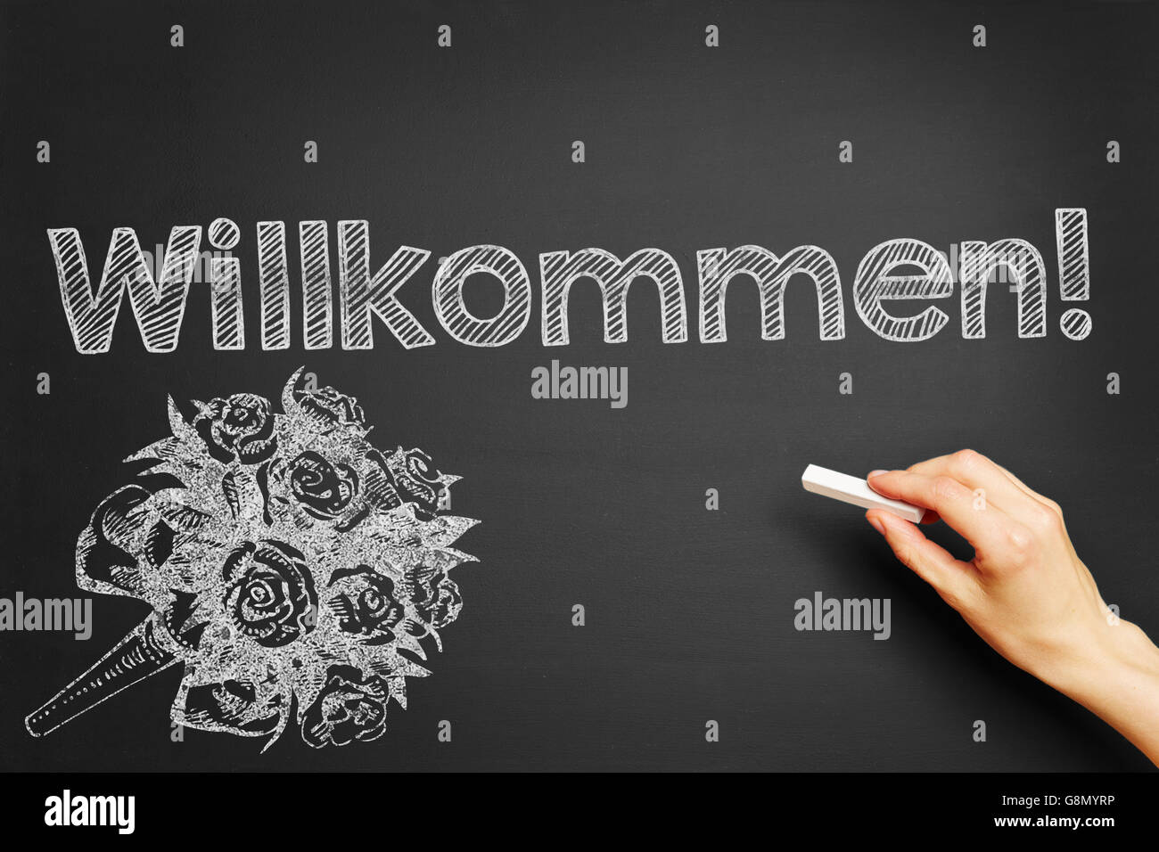 Hand writes in German 'Willkommen!' (Welcome!) on blackboard Stock Photo