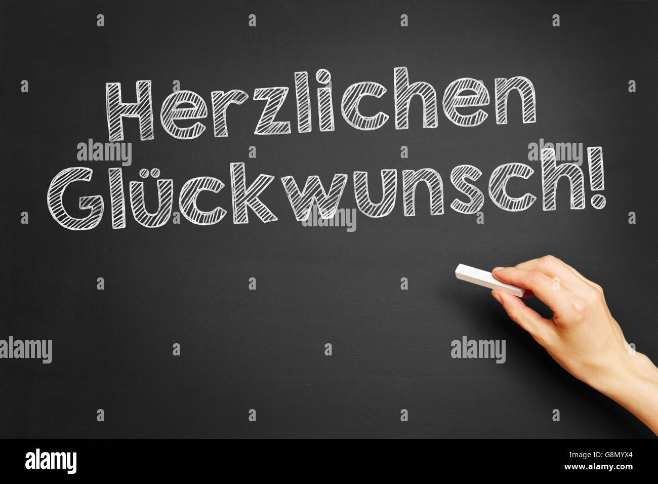 Hand writes in German 'Herzlichen Glückwunsch!' (Congratulations) on blackboard Stock Photo