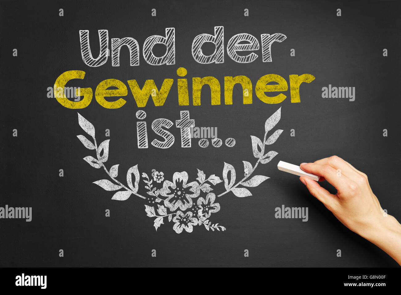 Hand writes in German 'Und der Gewinner ist...' (And the winner is...) on blackboard Stock Photo