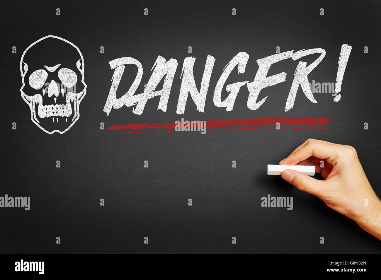 Hand with chalk writing 'Danger!' on a blackboard Stock Photo