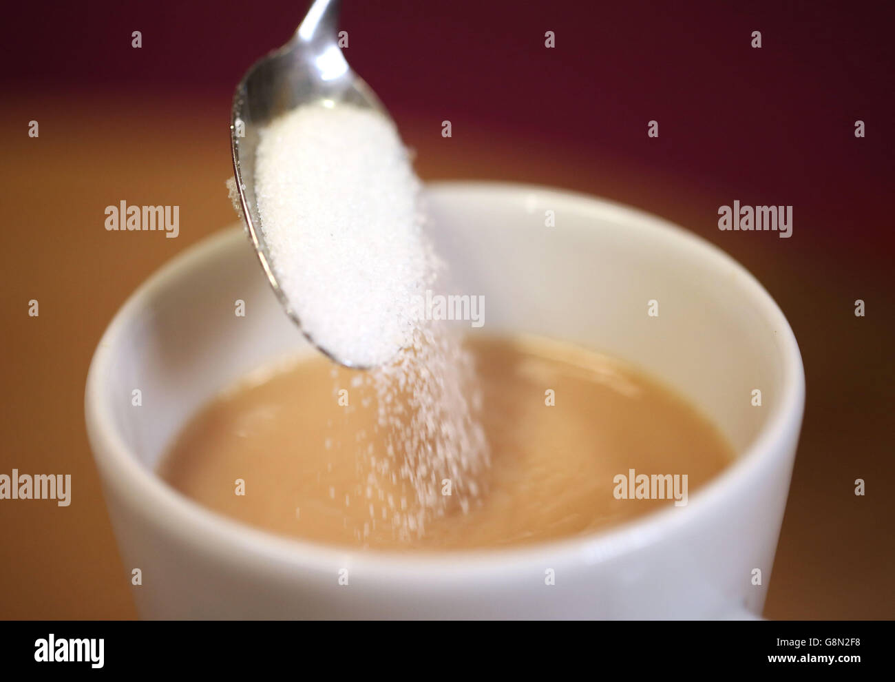 A teaspoon of sugar being poured into a cup of tea as there are