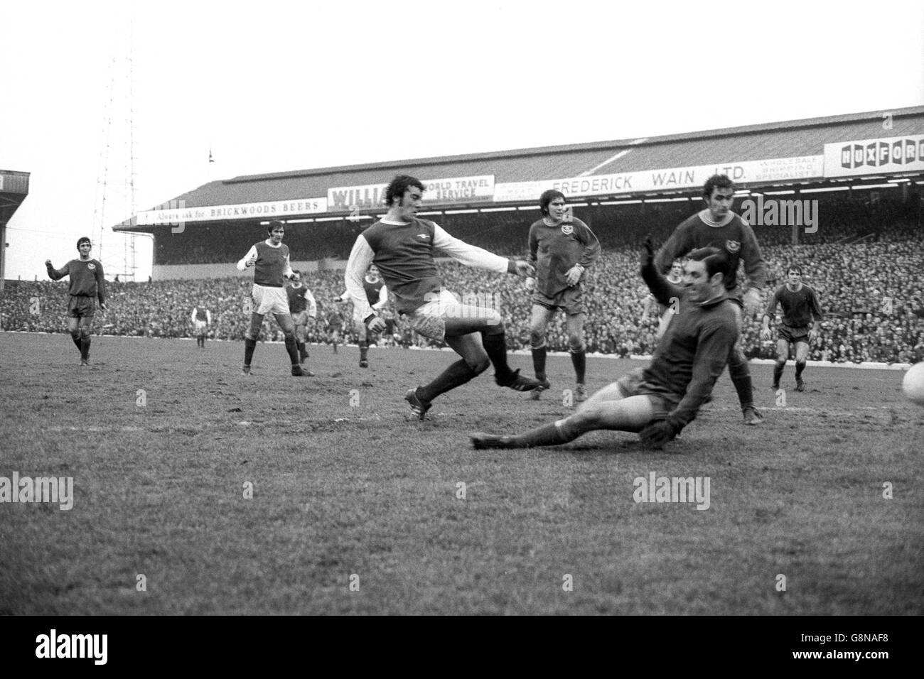 Portsmouth goalkeeper John Milkins slides as he confronts prancing No.10 Ray Kennedy during the fourth round FA Cup tie at Fratton Park. Behind Milkins is Portsmouth No.5 Colin Blant. Stock Photo
