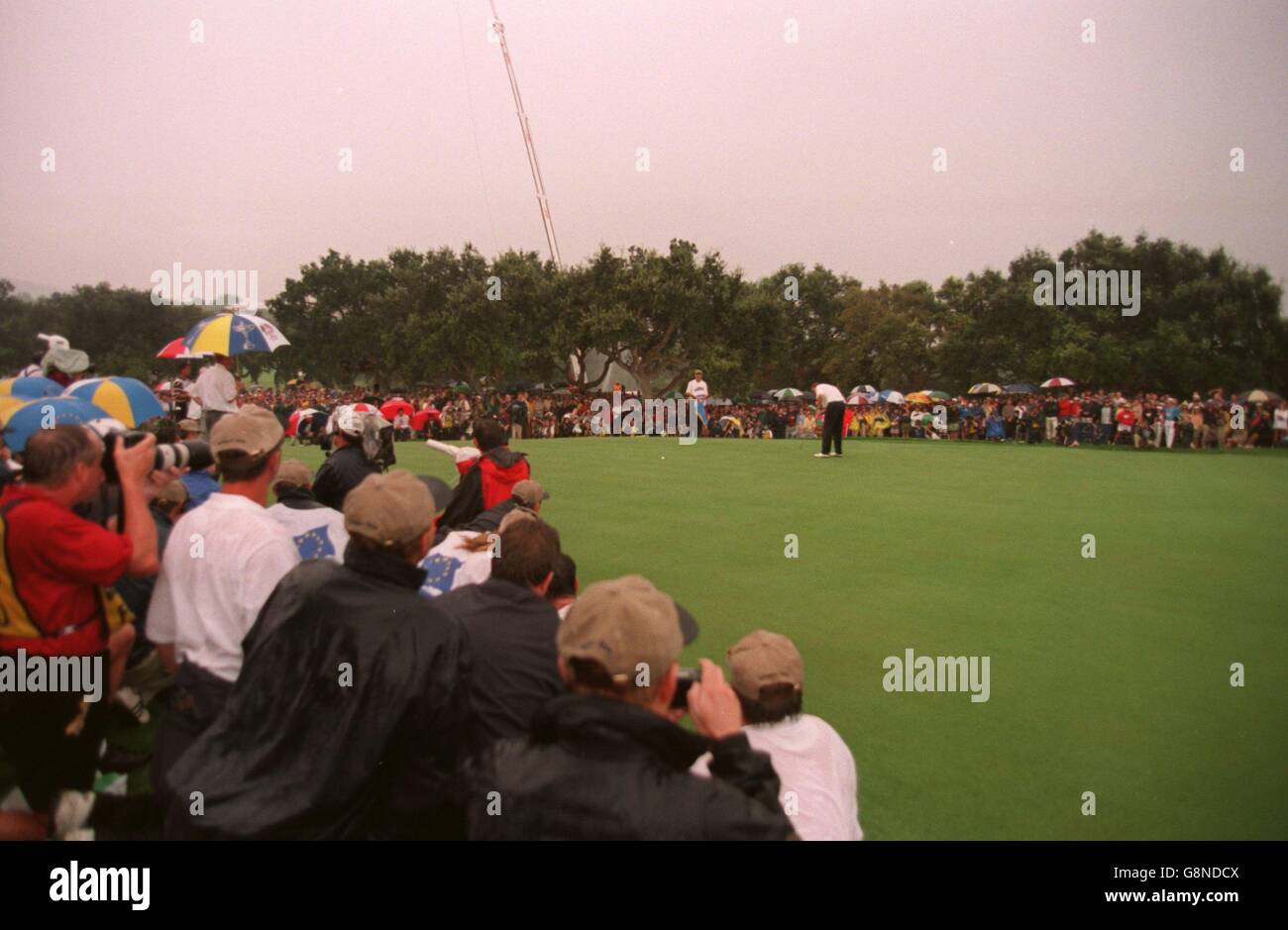 Golf - Ryder Cup - Europe v USA - Valderrama Golf Club, Spain. Europe's Colin Montgomerie putts at the eighteenth hole to win the match as the media and players crowd in Stock Photo