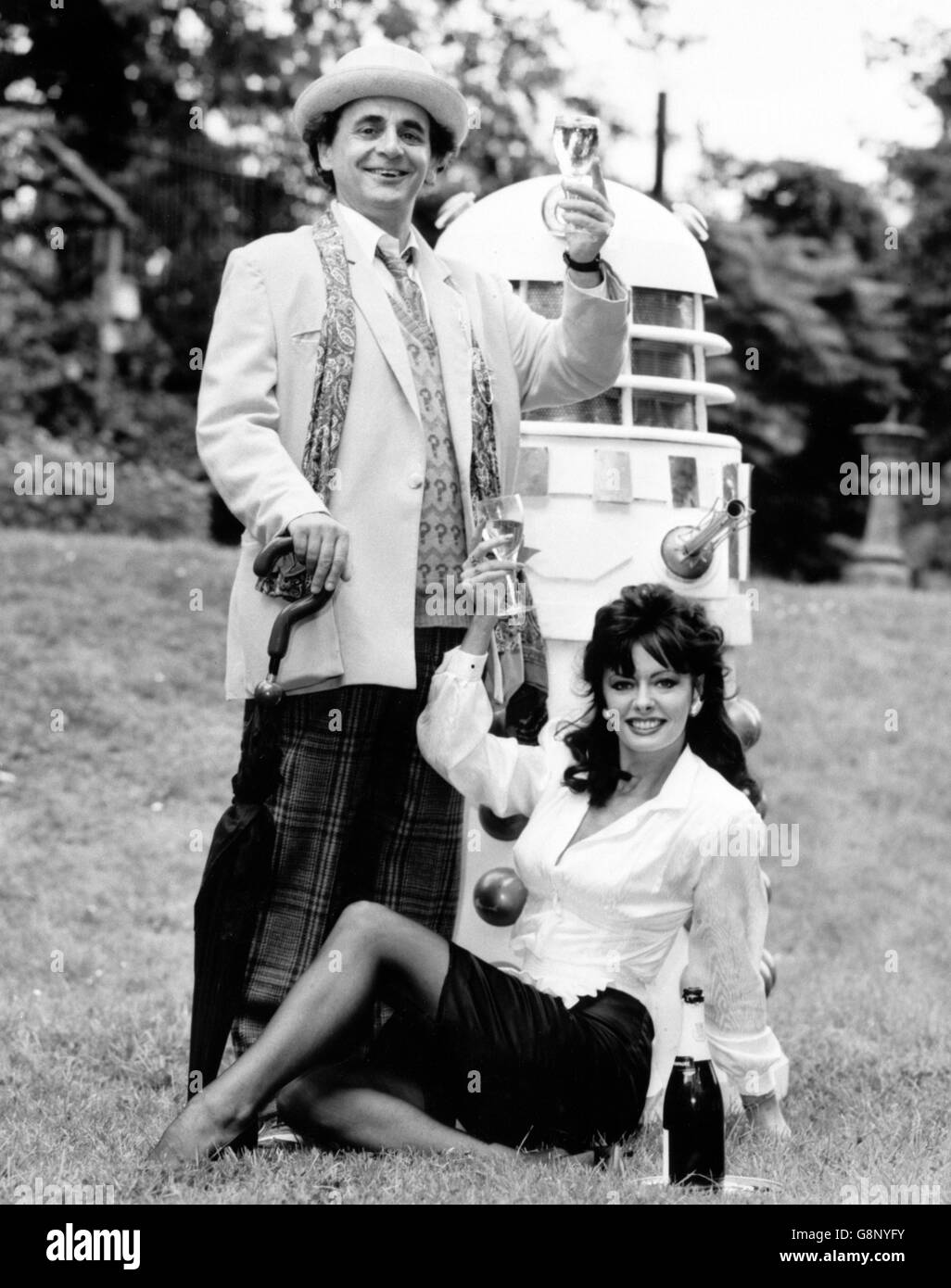 Eccentric Time Lord Doctor Who (played by actor Sylvester McCoy) toasts the television's programme's 25th birthday with 'Allo 'Allo! favourite waitress Yvette (actress Vicki Michelle), watched over closely by one of the Doctor's oldest enemies, a Dalek. Stock Photo