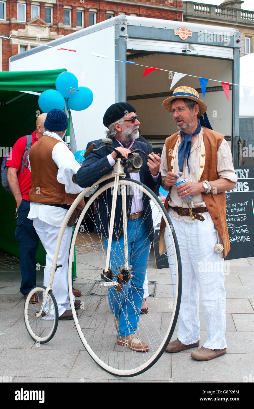 Penny Farthing bicycle and two men in old fashioned costume talking to each other. Stock Photo