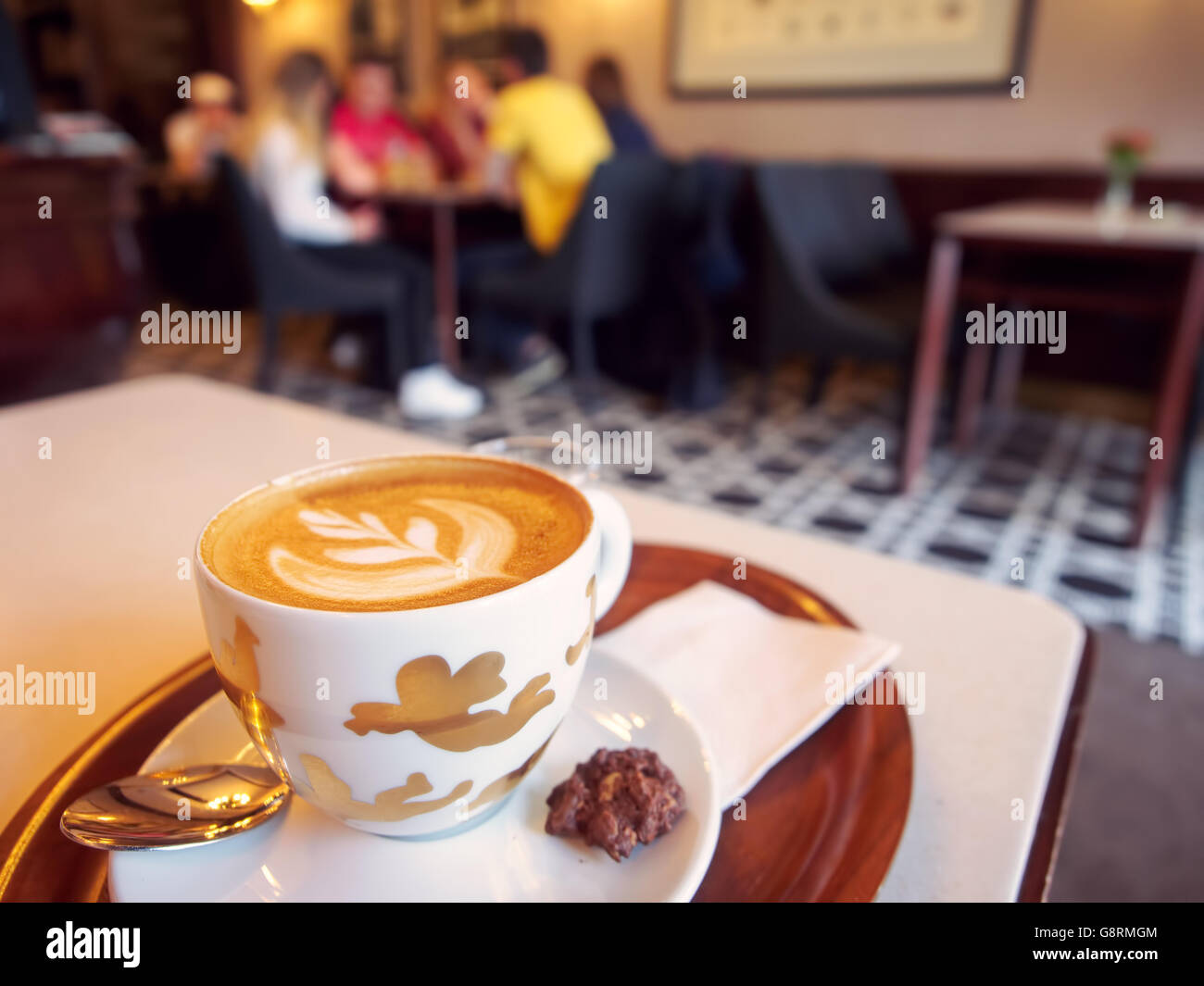 Cup of cappuccino in cafeteria with people in blurred background Stock Photo