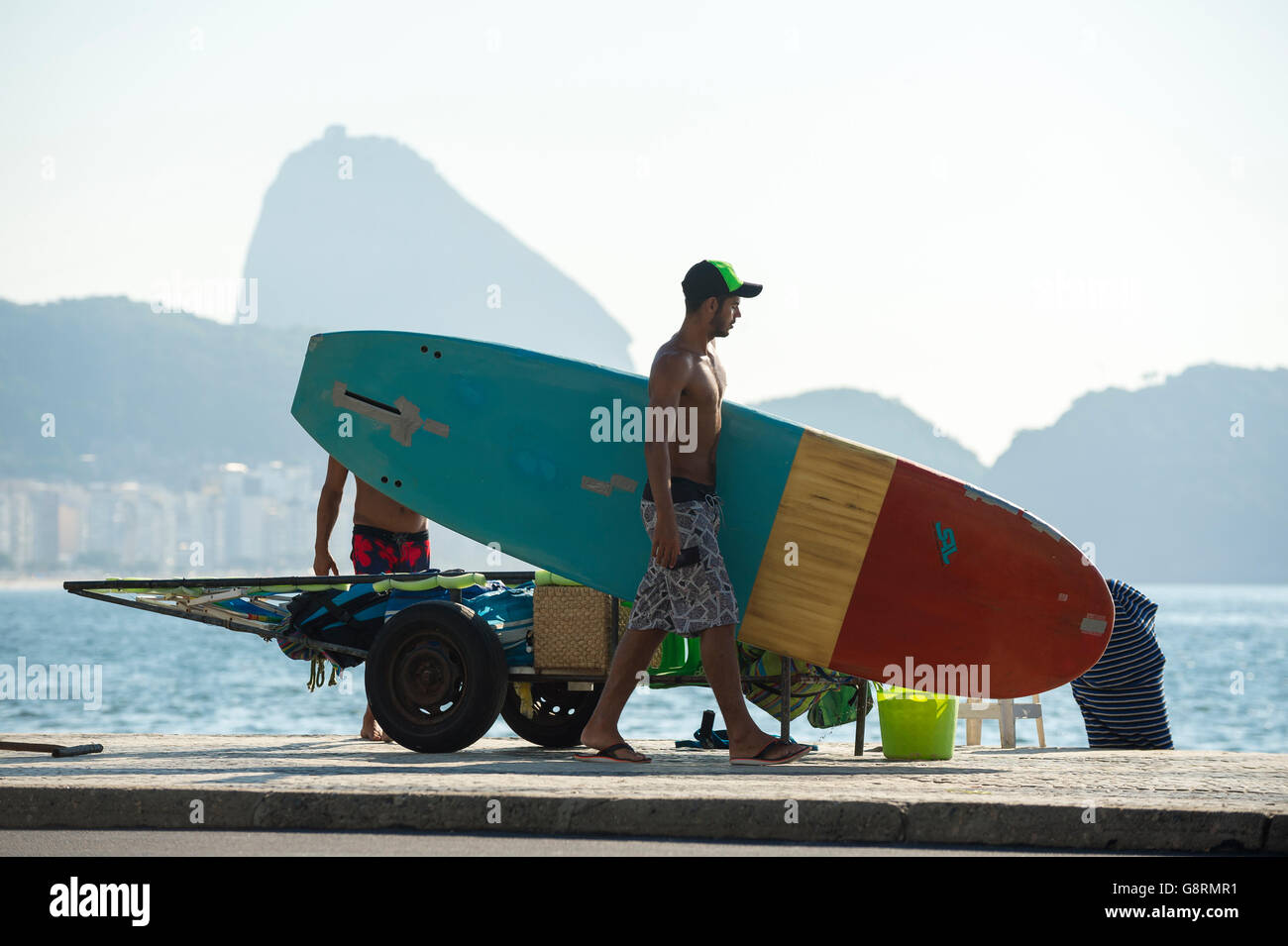 RIO DE JANEIRO - APRIL 5, 2016: Young carioca Brazilian man unpacks a stack of stand up paddle surfboards on Copacabana Beach. Stock Photo