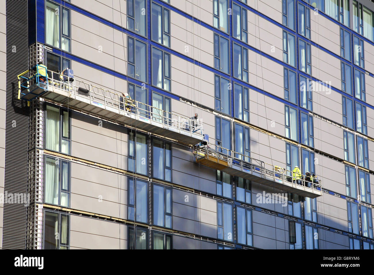 construction workers use suspended access platforms to install ceramic tiles to the facade of a new hotel in London, UK Stock Photo