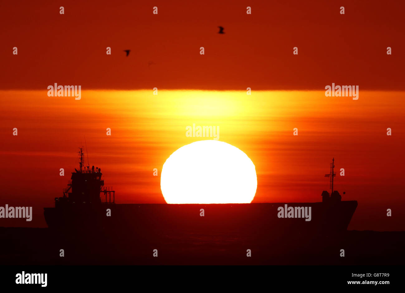 A ship out in the North Sea waits to enter the River Tyne on the North east coast as the sun rises. Stock Photo