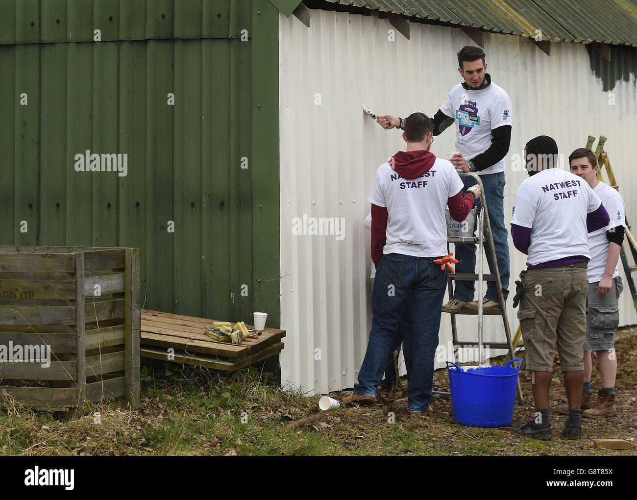 NatWest staff paint an outbuilding during a photocall at Dymock Cricket Club in Gloucestershire. Stock Photo