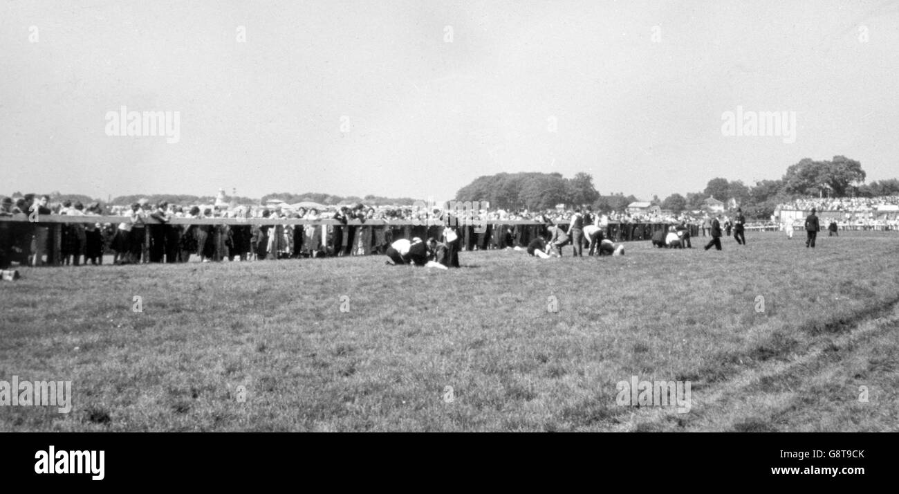 Helpers tend to injured jockeys lying on the turf, watched by race-goers crowding the rail, after seven horses had fallen in a pile up near Tattenham Corner during the Derby at Epsom. Stock Photo