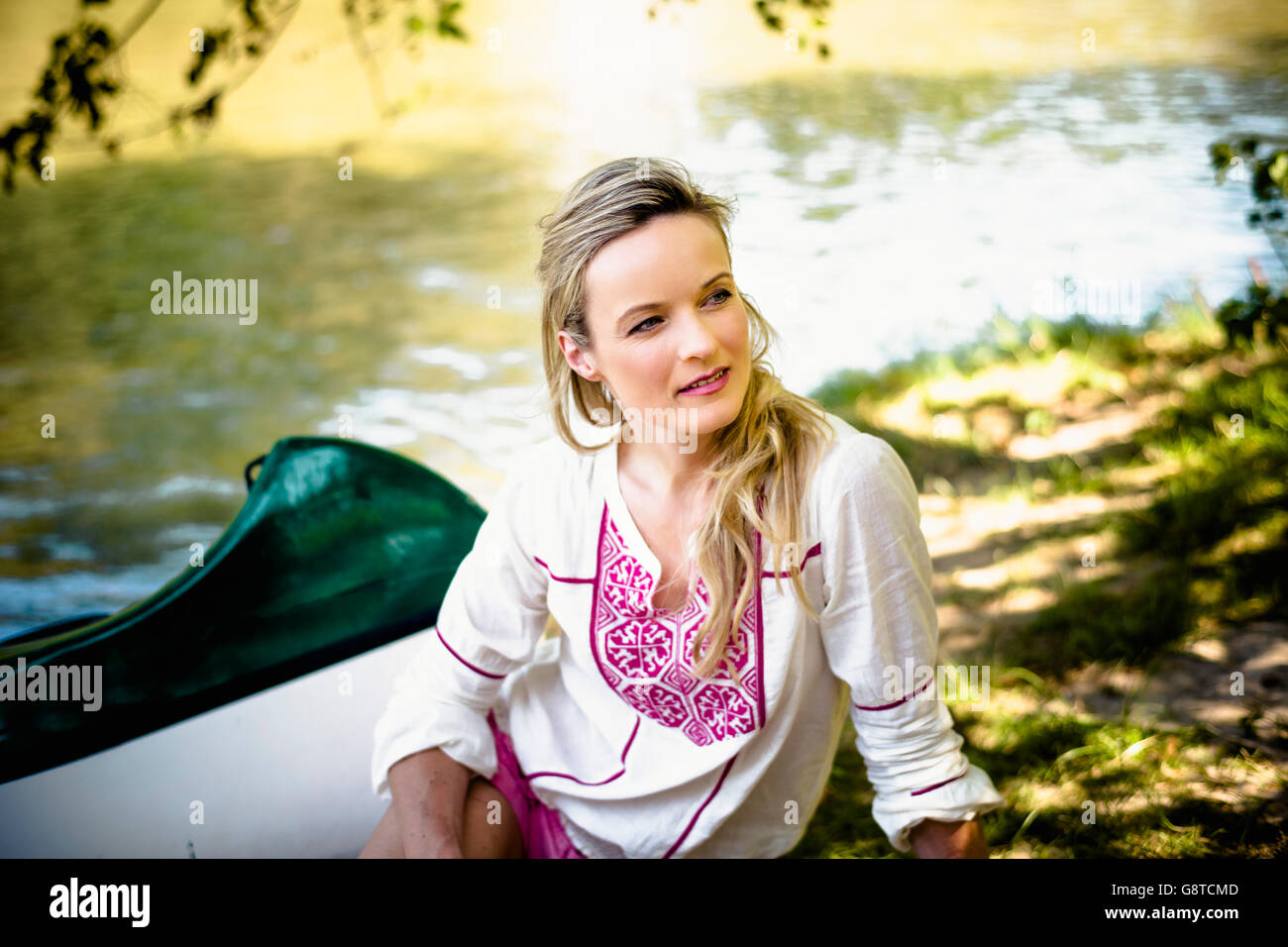 Young woman sits on the riverside, foothills of the Alps, Bavaria, Germany Stock Photo