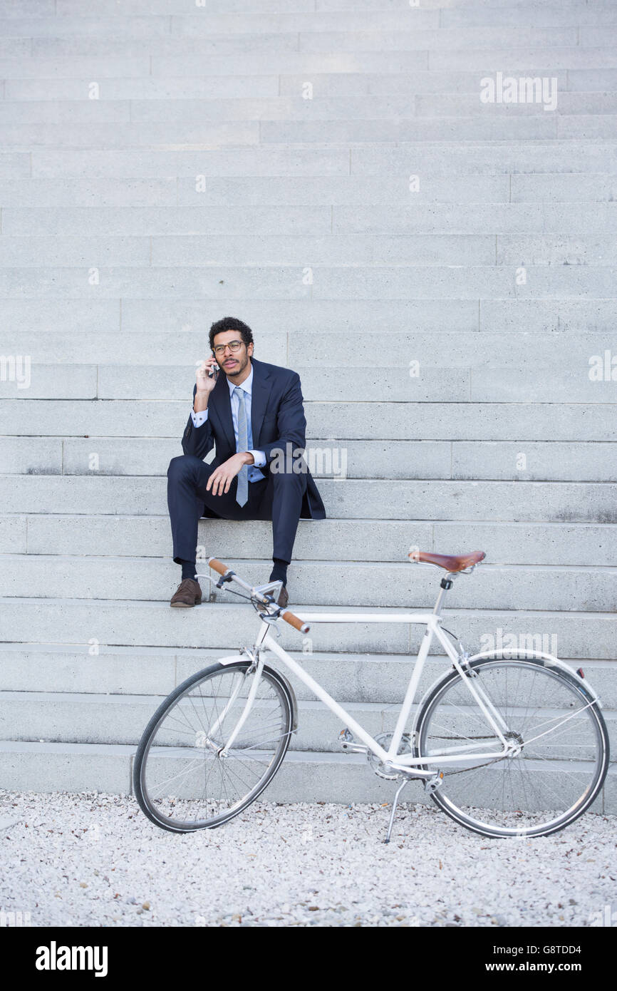Businessman with bicycle using phone in city Stock Photo
