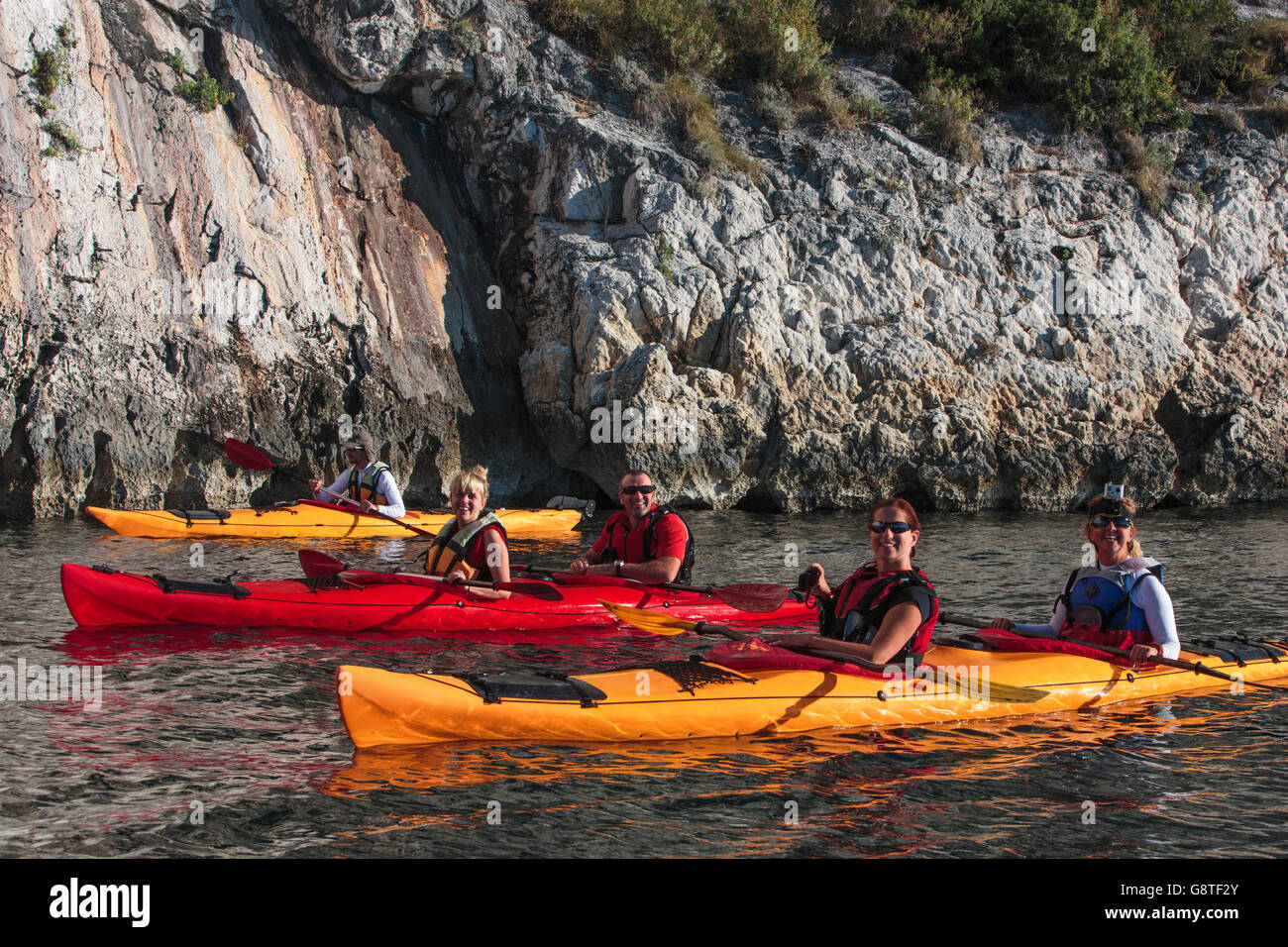 Group of people kayaking next to rock formation Stock Photo