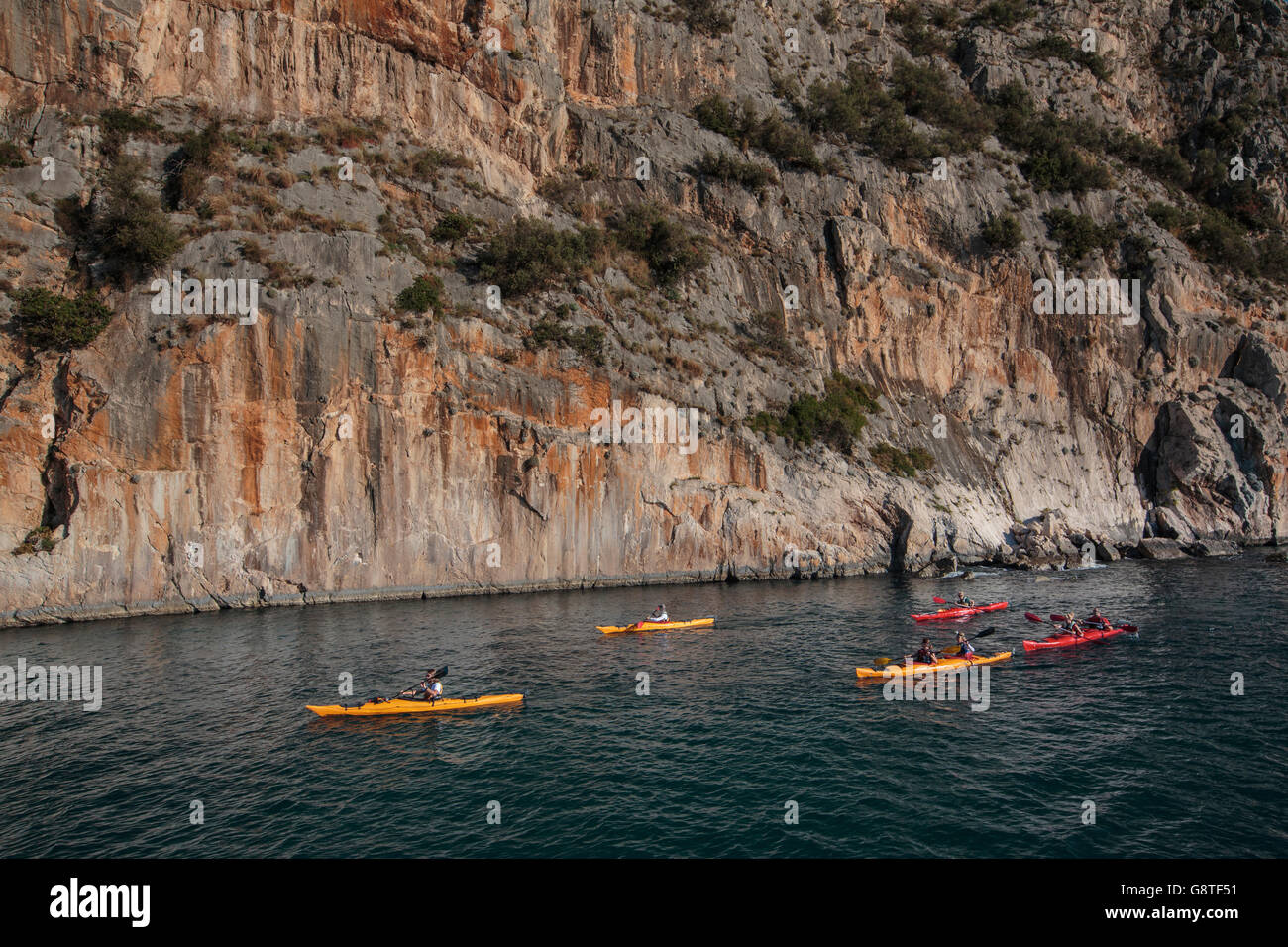 Group of people kayaking next to rock formation Stock Photo
