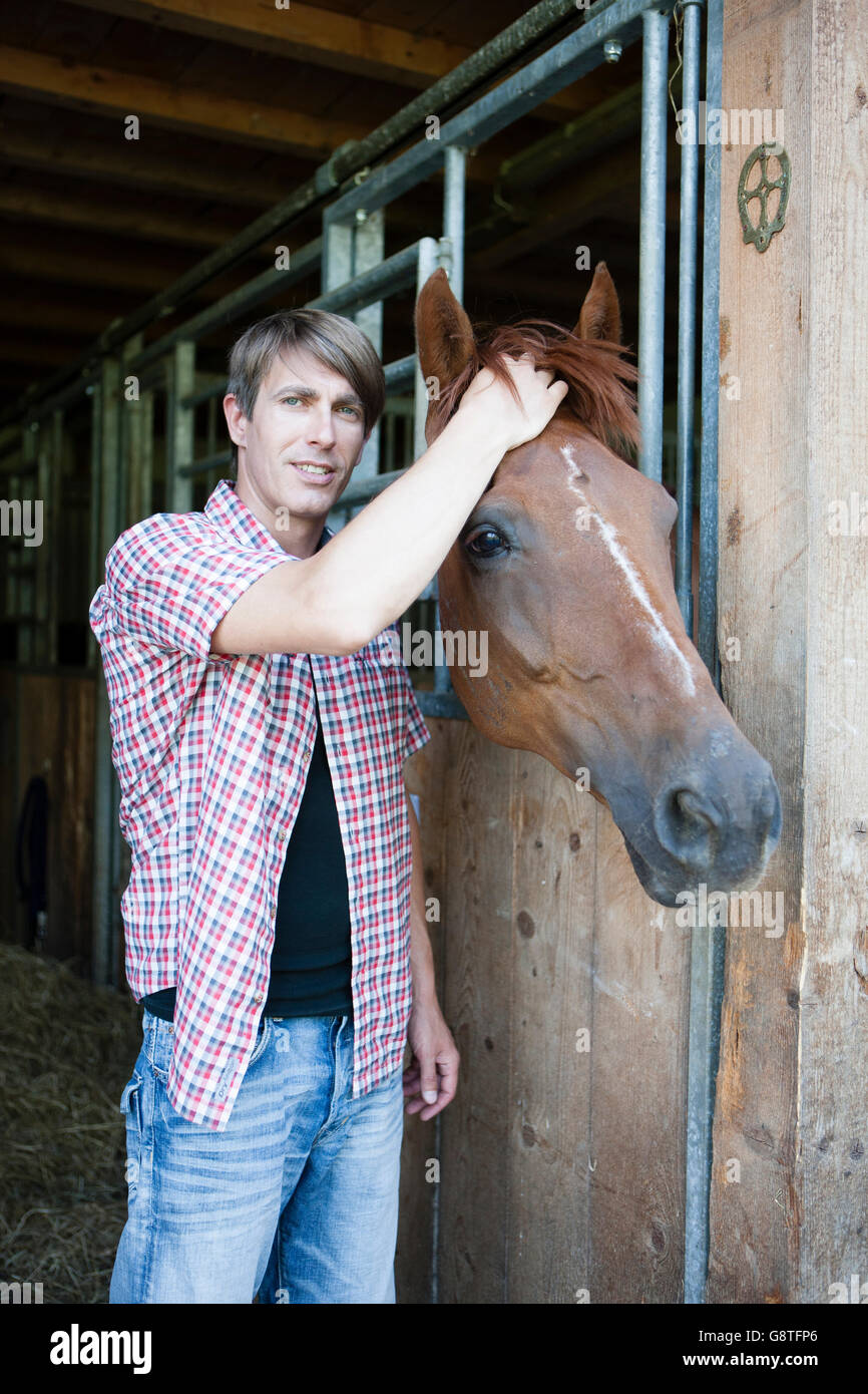 Man in stable stroking horse Stock Photo