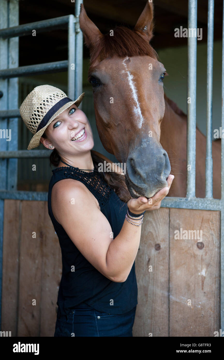 Woman with straw hat in stable feeding horse Stock Photo