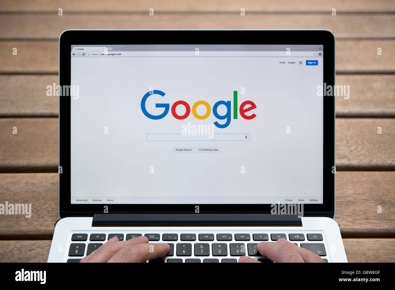 The Google website on a MacBook against a wooden bench outdoor background including a man's fingers (Editorial use only). Stock Photo