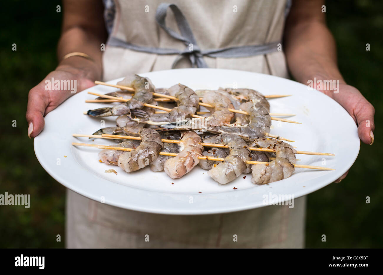 A woman is holding a plate of shrimp that are on skewers and ready for grilling. Stock Photo