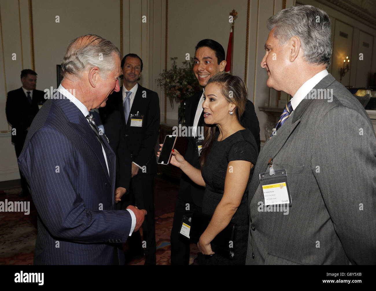 The Prince of Wales (left) reacts as Canadian television presenter Melissa  Grelo (second right) shows him an image of herself posing for a photograph  with Prince Harry, on a tour of Canada