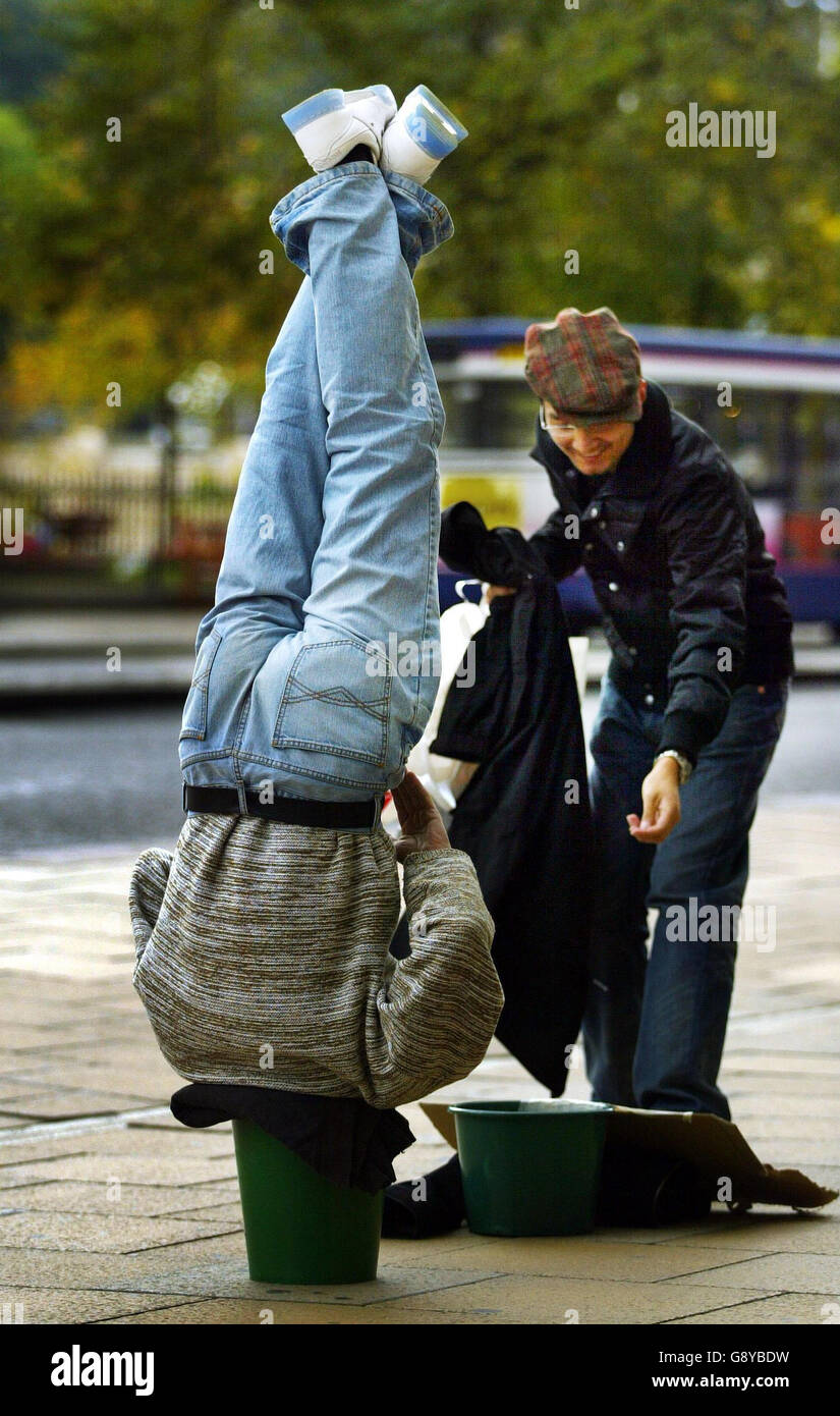 A homeless man stands on his head in a buckett attempting to raise money, in Princes Street