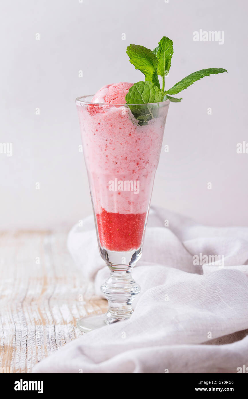 Glass of strawberry dessert with sorbet and mint, served over white wooden textured background with textile rag. Stock Photo