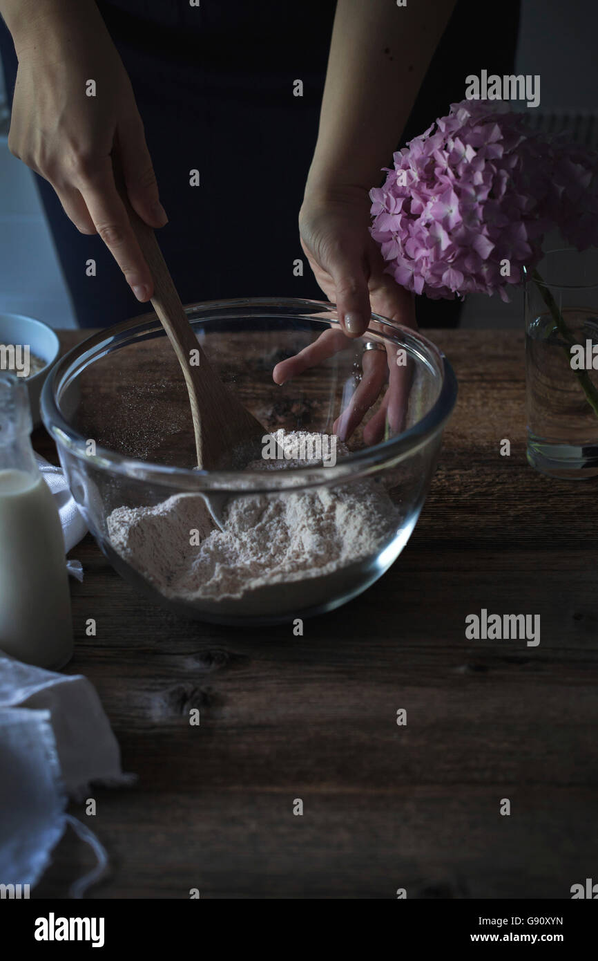 Hands mixing flour with a wooden spoon in a bowl on a rustic wooden table Stock Photo