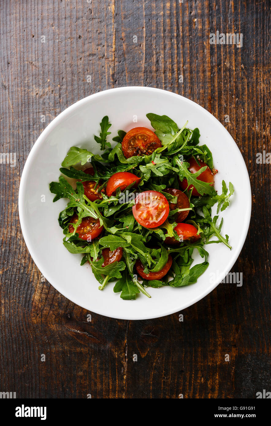 Salad with Cherry tomatoes and Arugula in white bowl on wooden background Stock Photo