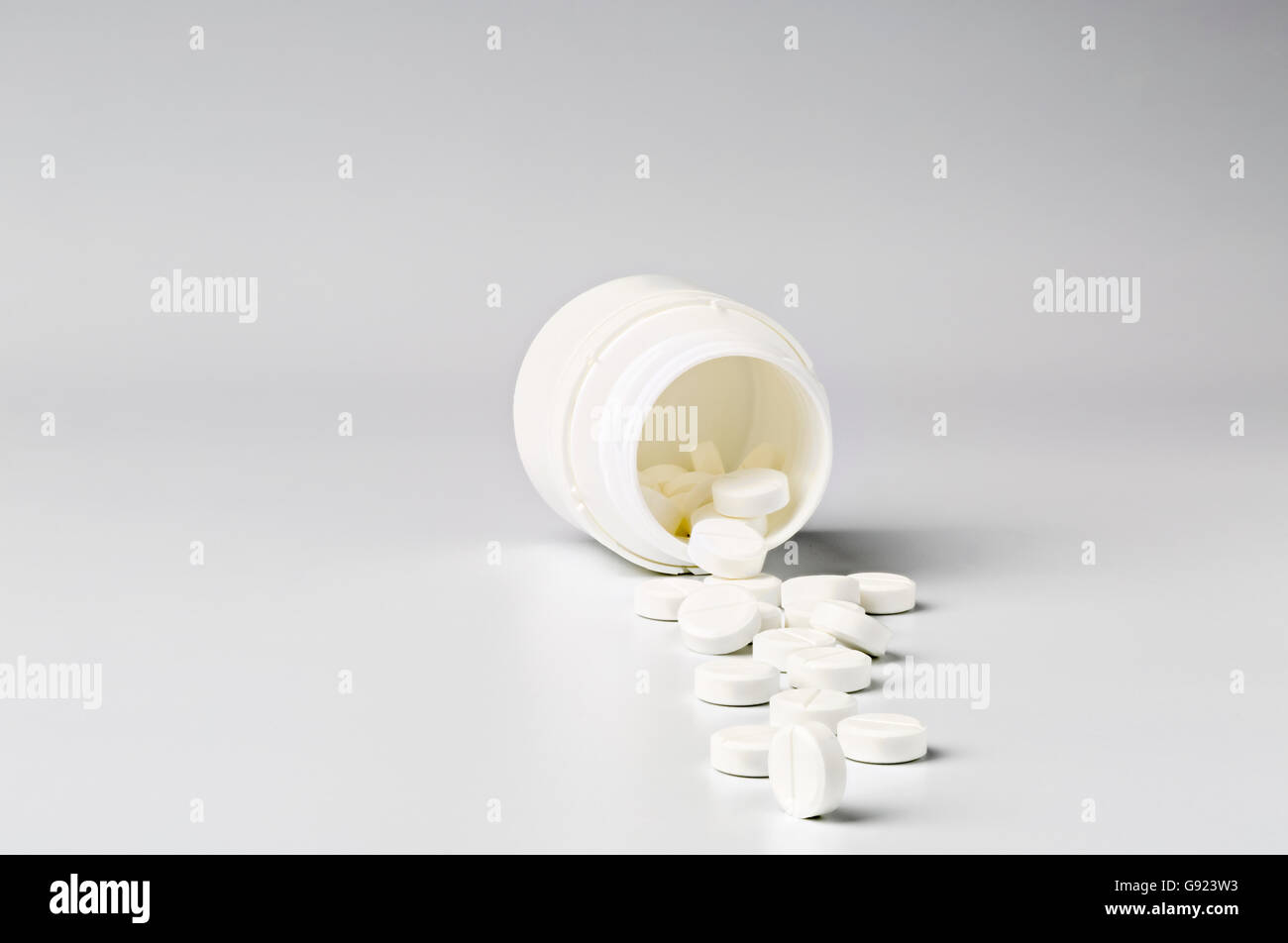 White plastic pill bottle and heap of round white pills Stock Photo