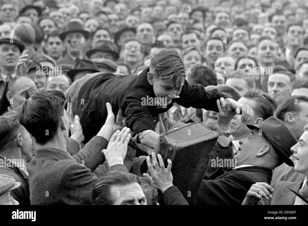 A young fan is passed over the heads of the crowd to a better viewing position at the front of the terrace. Stock Photo