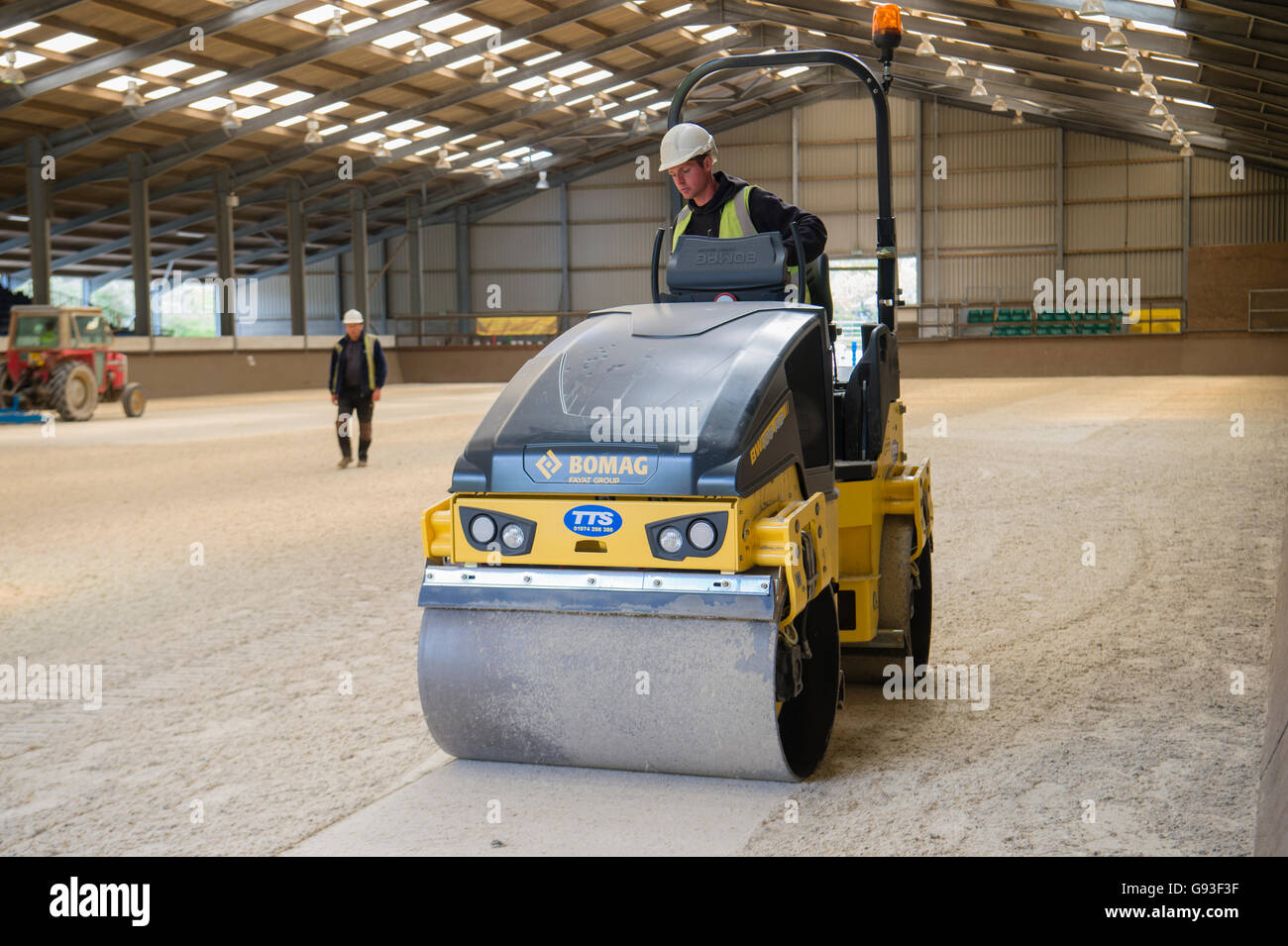 Heavy plant contract hire: A man operating a motorised mechanical roller machine preparing the new surface of an indoor equine riding centre, at Aberystwyth University, Wales UK Stock Photo