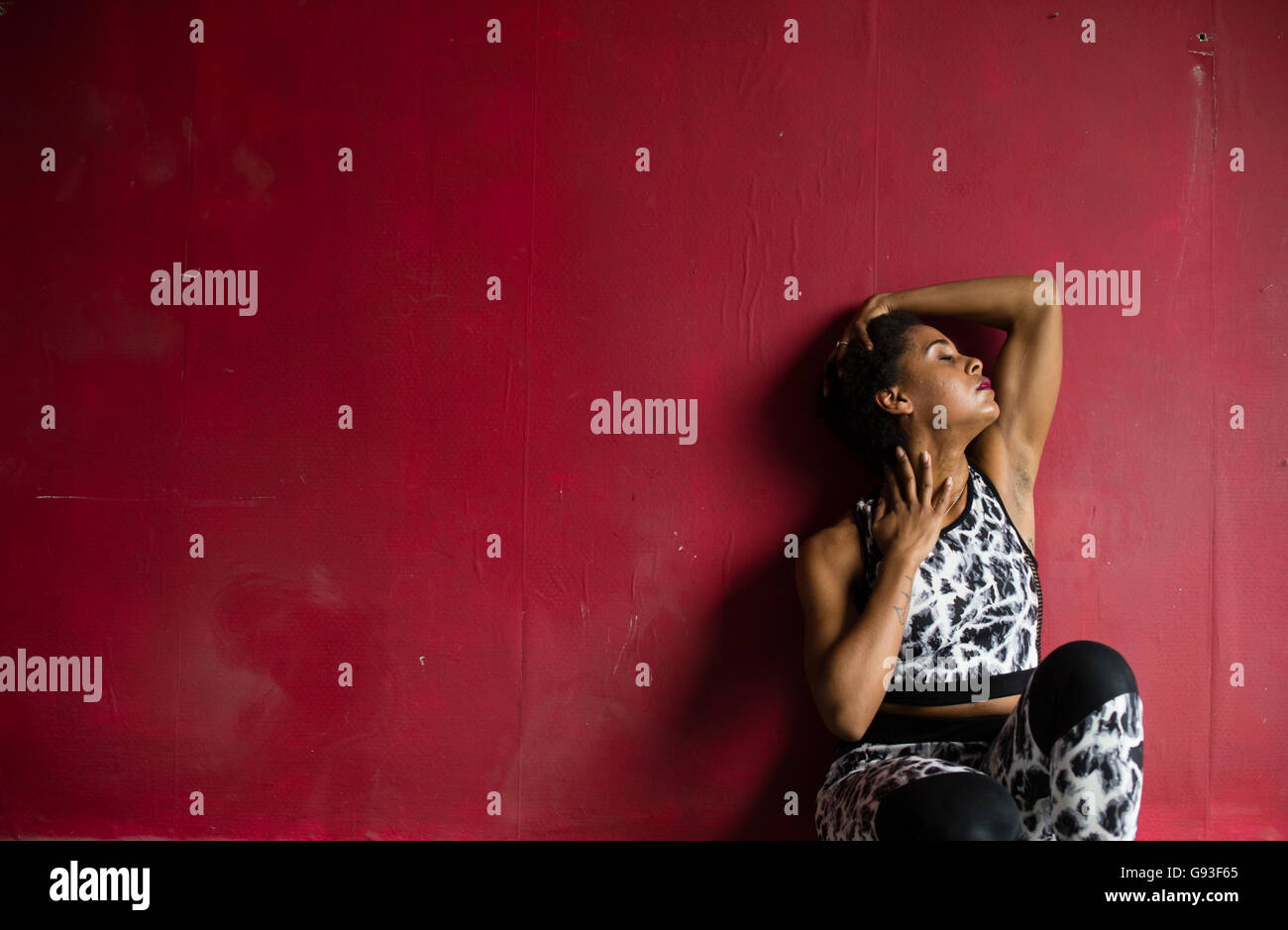 Beauty in dereliction : Fashion photography of a young afro-caribbean woman girl alone in a  red walled room  wearing fitness-style clothes, looking hot, sultry and moody Stock Photo