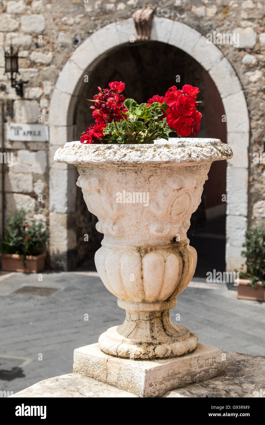 Red flowers planted in stone pot framed by stone archway Stock Photo