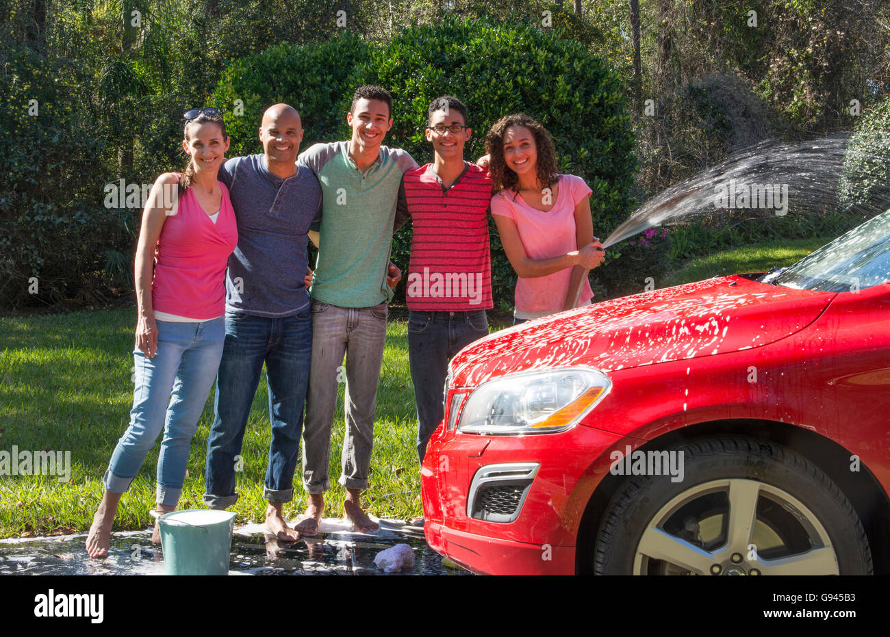 Family wash car portrait at home black Caribbean dad mom sons and daughter outside in sun red car fun together love Model Releas Stock Photo