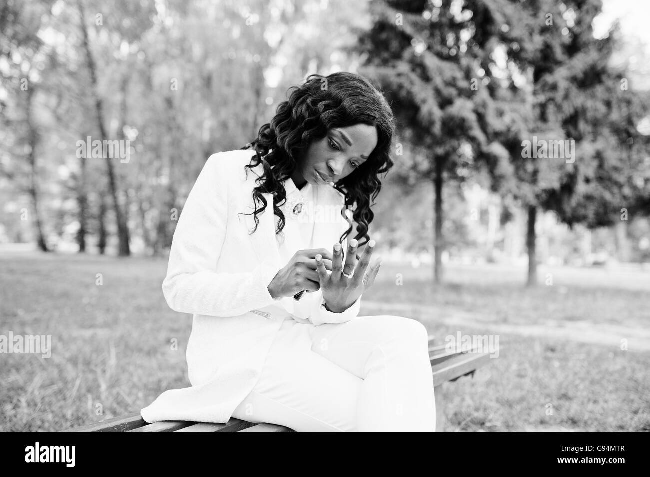 Portrait of pretty black african american girl sitting on bench at green park and showing her engagement ring at finger Stock Photo