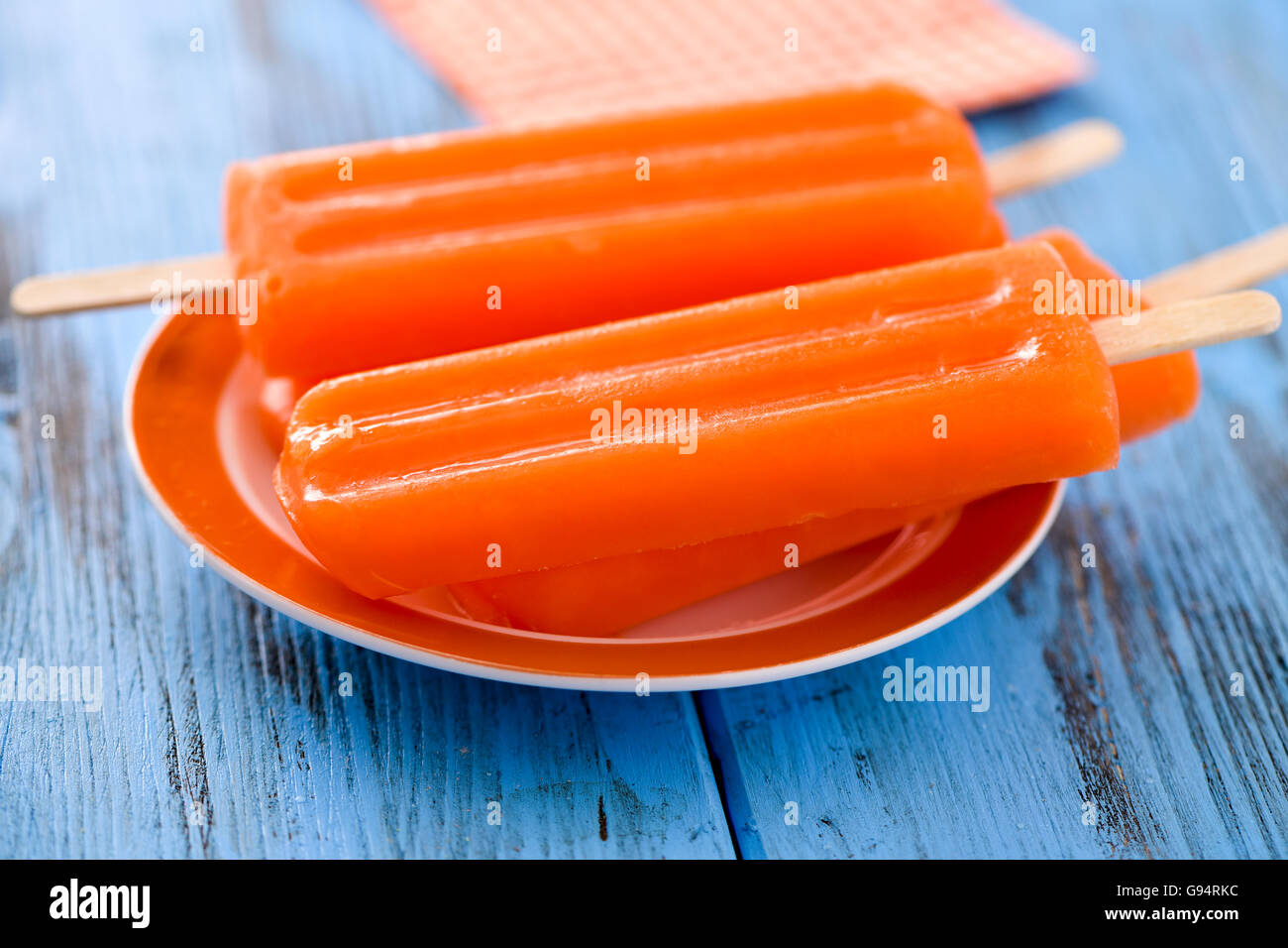 two refreshing orange flavored ice pops in a plate, on a blue rustic wooden table Stock Photo