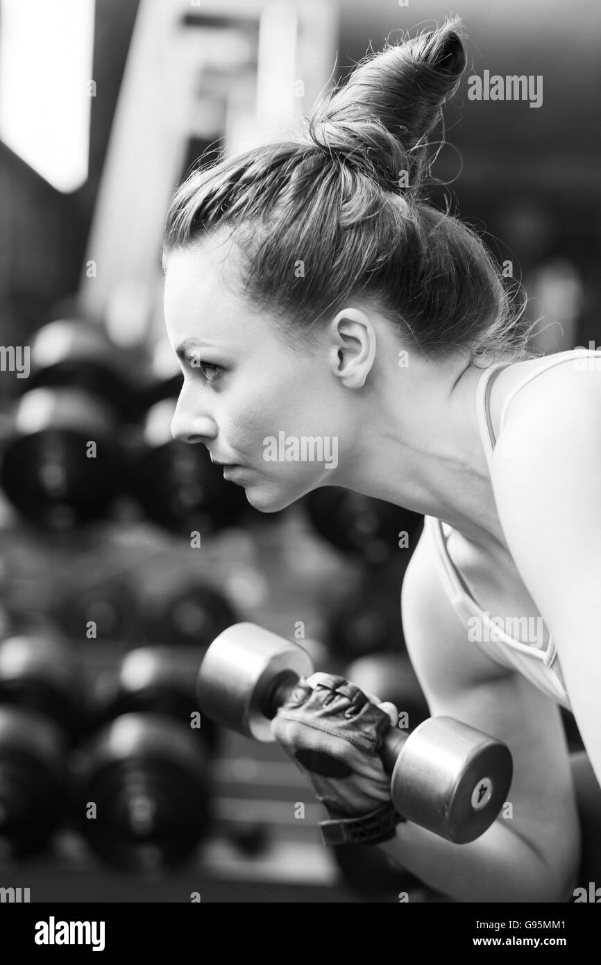 Young confident woman doing biceps curl exercise with dumbbells in fitness center. Slim girl training in the gym with dumbbells. Stock Photo