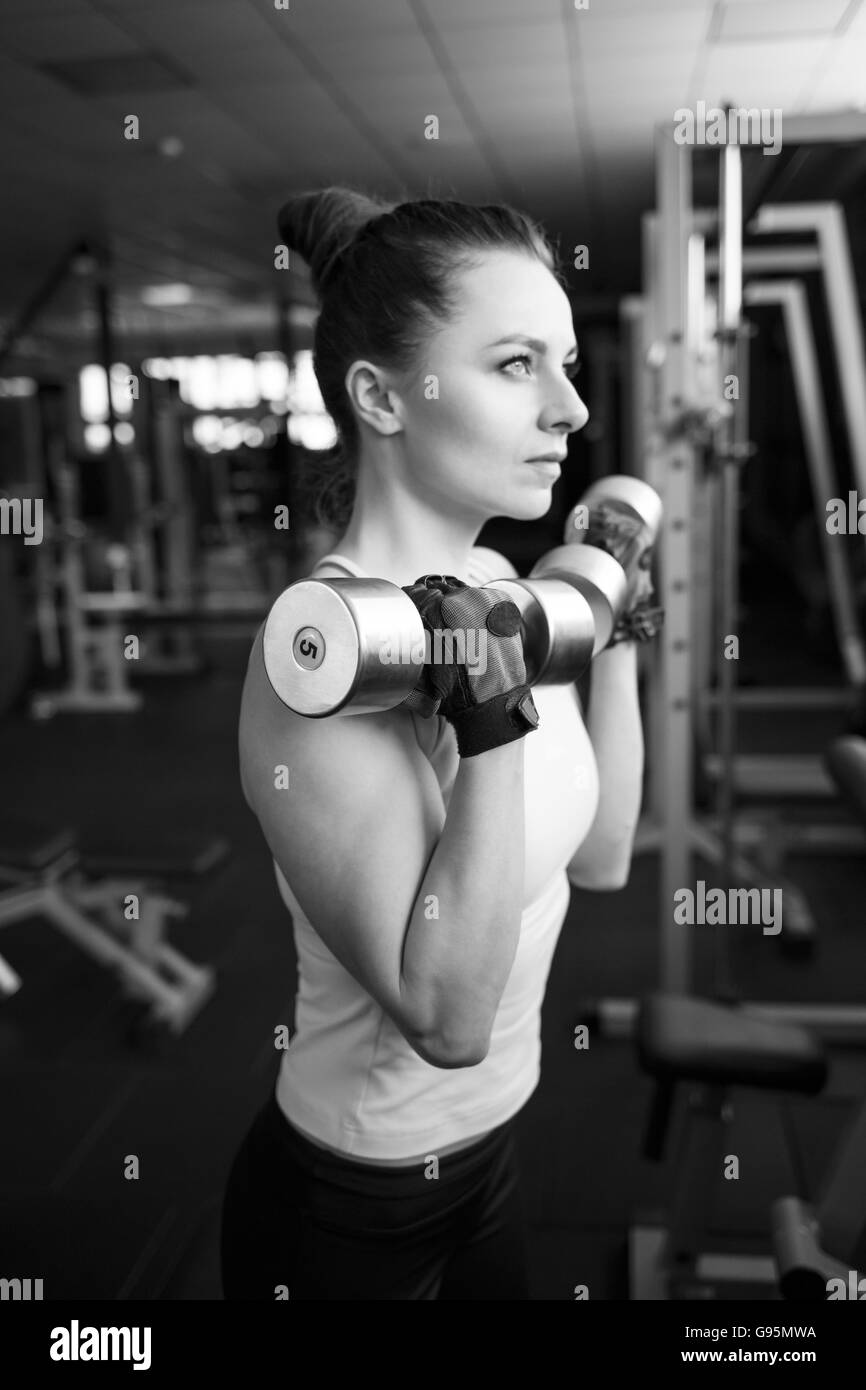Young confident woman doing biceps curl exercise with dumbbells in fitness center. Slim girl training in the gym with dumbbells Stock Photo