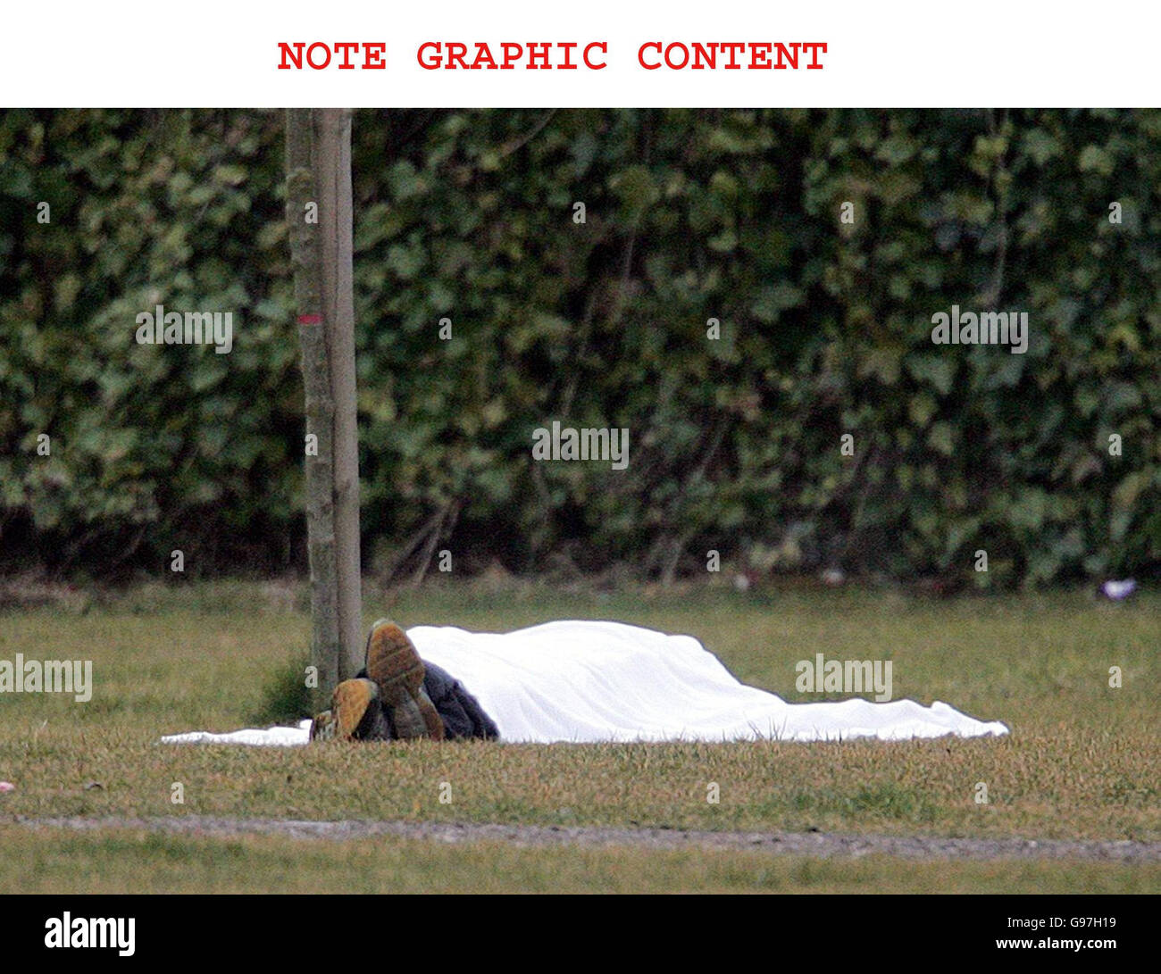 NOTE GRAPHIC CONTENT. A covered body lies in a patch of wast ground
