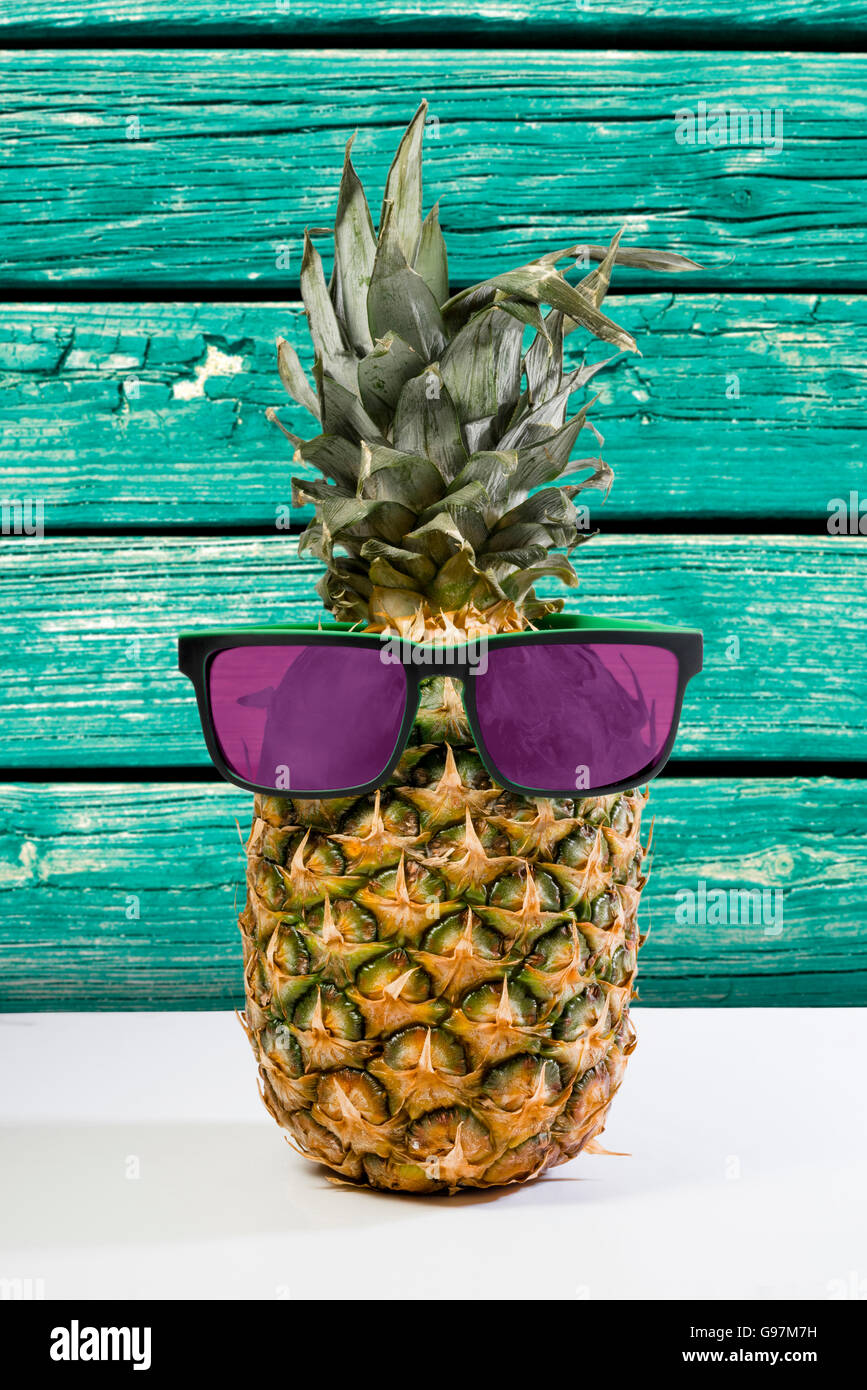 Trendy summer pineapple wearing hipster style sunglasses with beach wood texture color background. Stock Photo