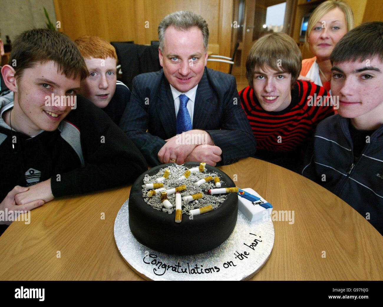 Scottish First Minister Jack McConnell (centre) is accompanied by Dumbarton Academy students (l-r); Andrew McWatt, Steven Nelson, Andrew Ferguson and Ian Green and youth worker Karen Muir (back), as they sit in front of a smoking cake at the Scottish parliament in Edinburgh, Thursday March 23, 2006. The cake was presented to the First Minister by his staff to mark Scotland's smoking ban, which starts on Saturday night. PRESS ASSOCIATION Photo. Photo credit should read: David Cheskin / PA pool. Stock Photo