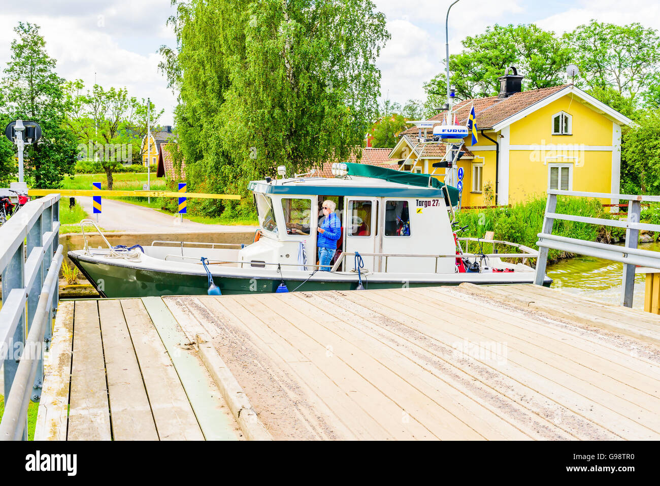 Loddby, Sweden – June 20, 2016: People in a small motorboat pass the open rolling bridge in the Gota canal. Woman standing in ca Stock Photo